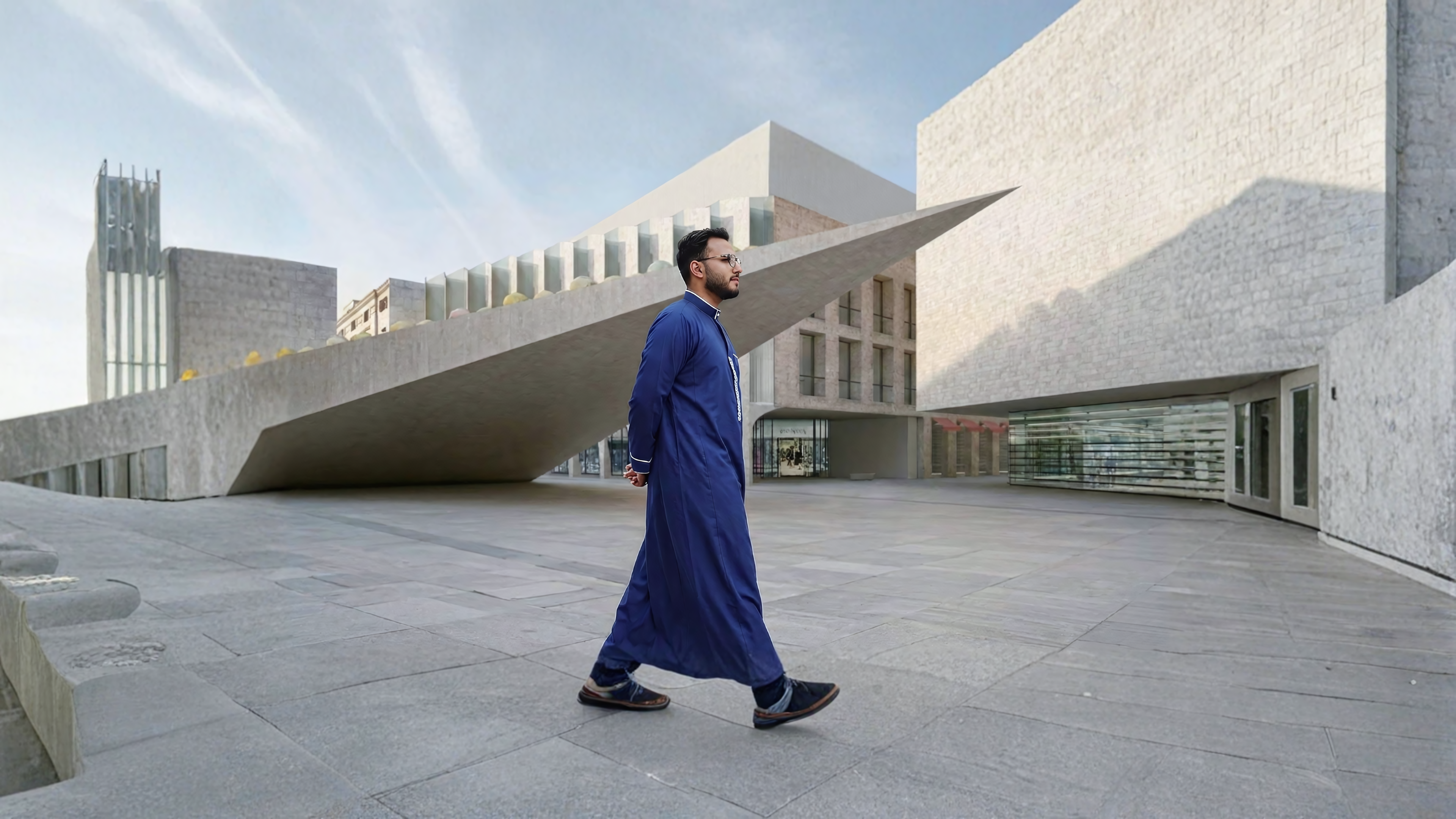 Man in traditional dark blue thobe walking through modern urban plaza with minimalist architecture in the USA
