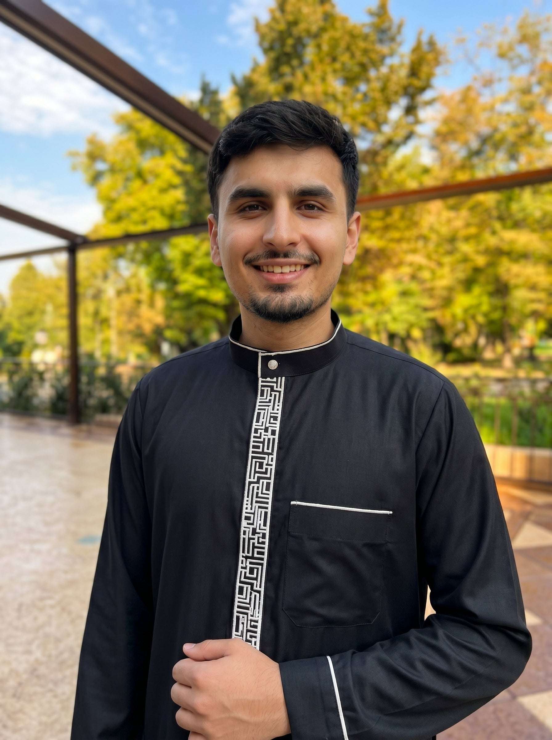 Black embroidered jubba with contrast detailing, leaning against a pergola