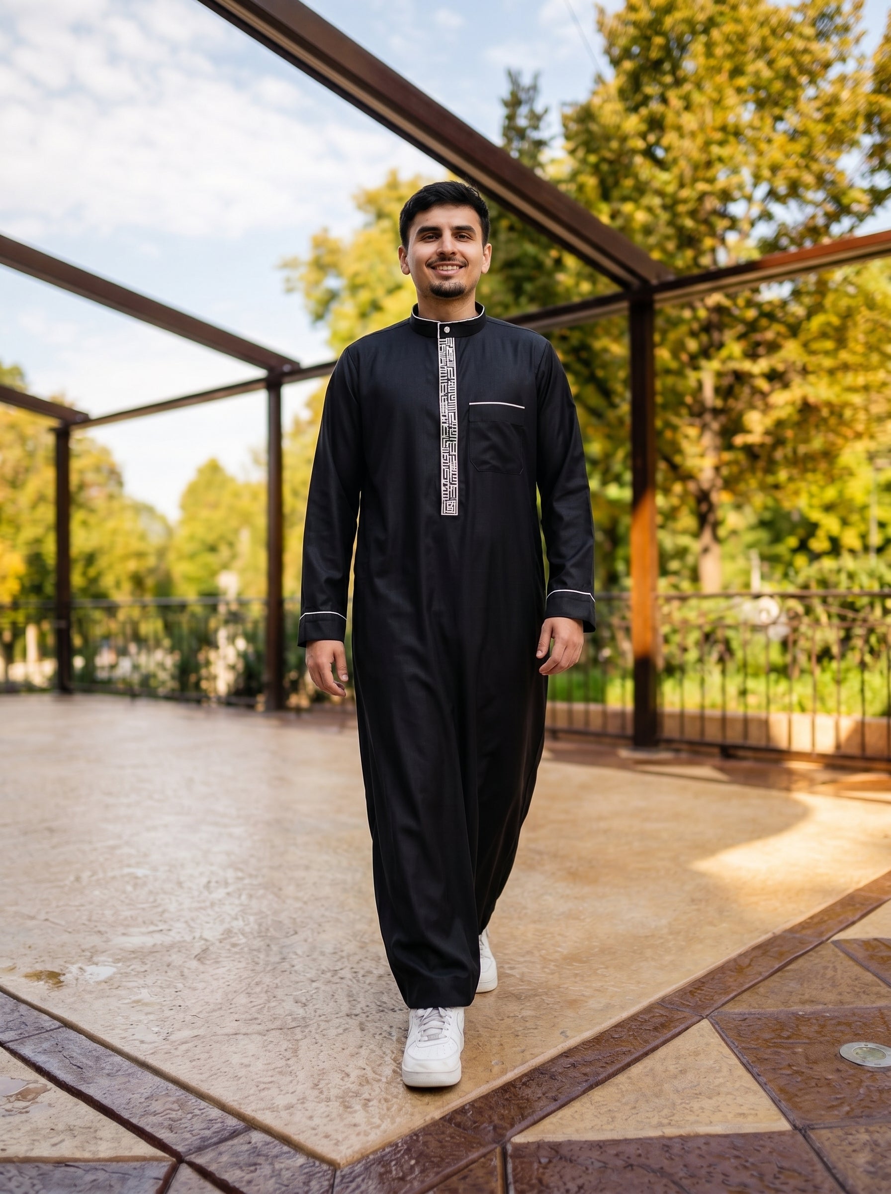 Premium black thobe with white trim walking shot on patio, inspired by Shukr clothing and Burda style, high-end Islamic menswear by The Topiwala Chicago USA collection.