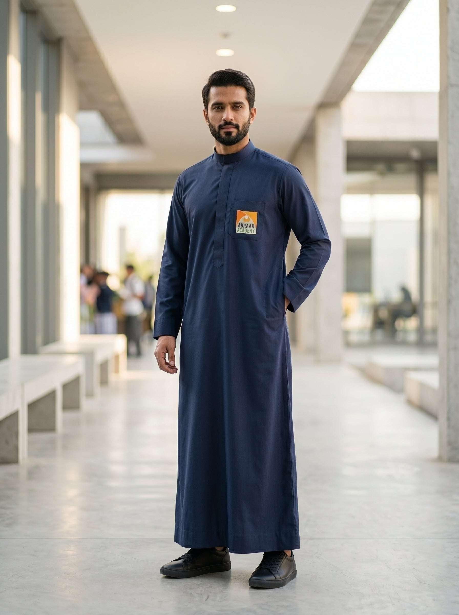 Adult male wearing the official Abraar Academy navy blue men's uniform thobe with chest logo, showcasing a tailored architectural fit in a modern setting.