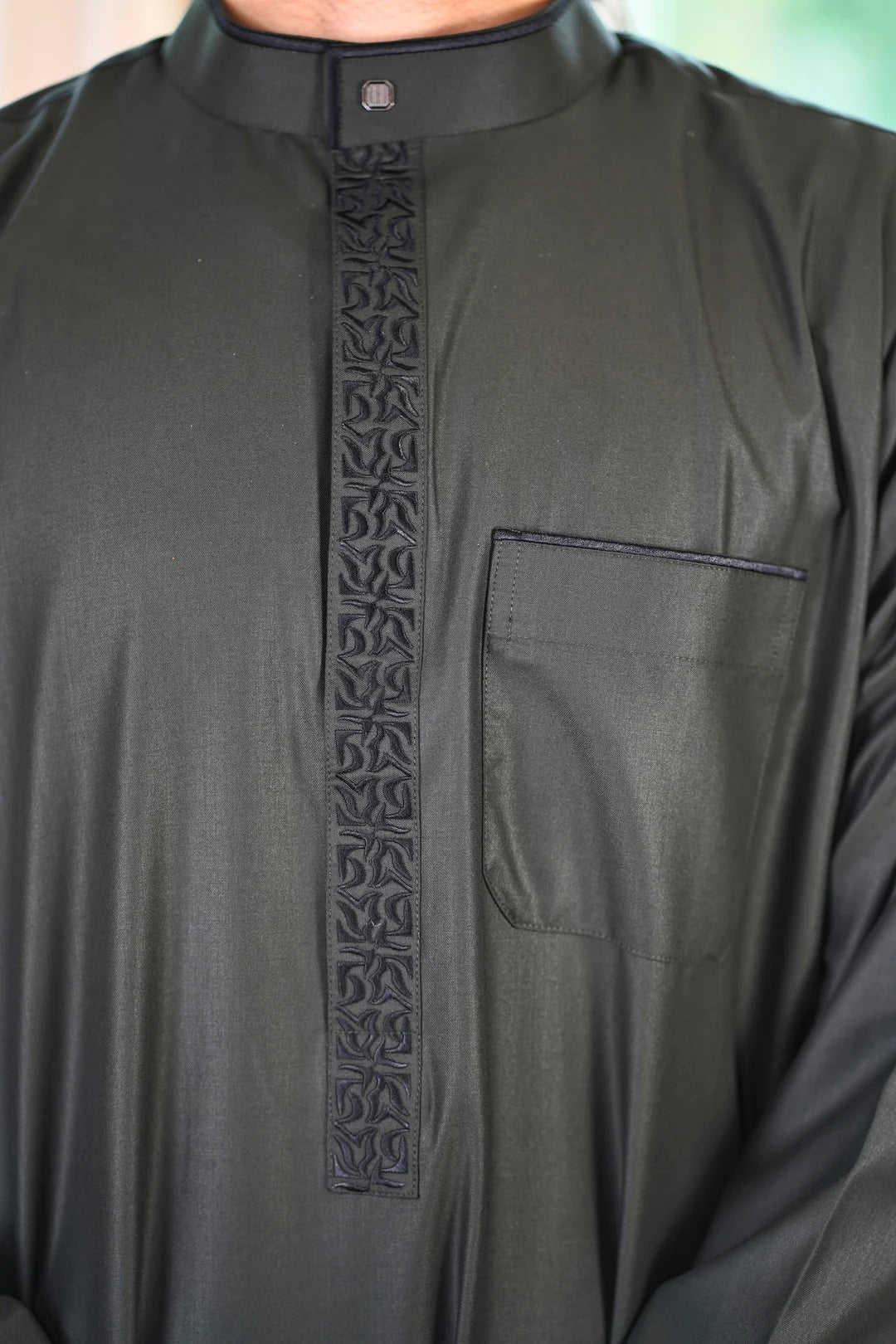 Close up of the intricate black embroidery on the chest and mandarin collar of the charcoal men's thobe