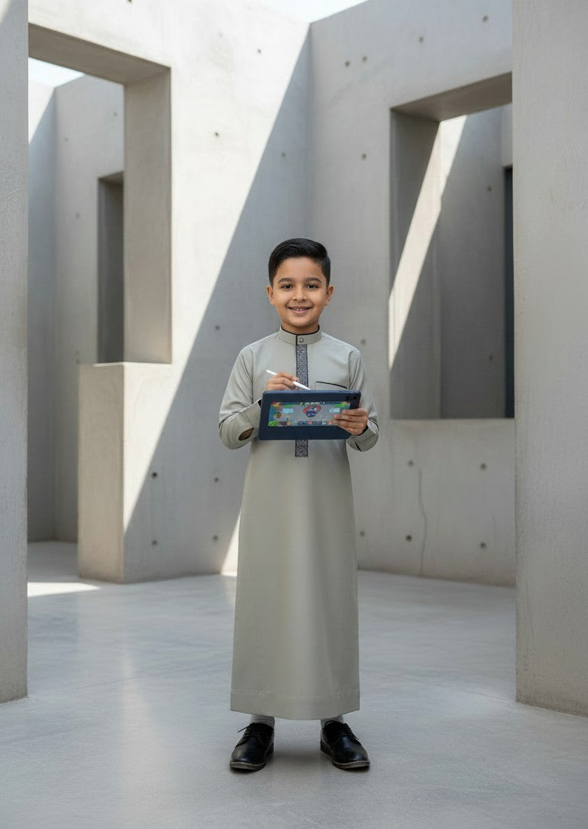 Boy sitting on a modern concrete bench reading a book, wearing a comfortable and tailored light grey kids jubba. Premium Islamic menswear aesthetic adapted for children, combining traditional modesty with modern design.
