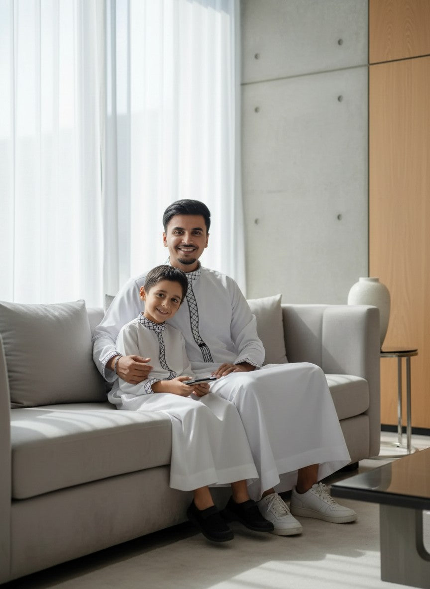 Comfortable white matching thobes for father and son relaxing at home. Breathable Islamic clothing, premium wrinkle-resistant jubbas for men and kids. Casual modest menswear, elegant family matching outfits, modern Sunnah style fashion.