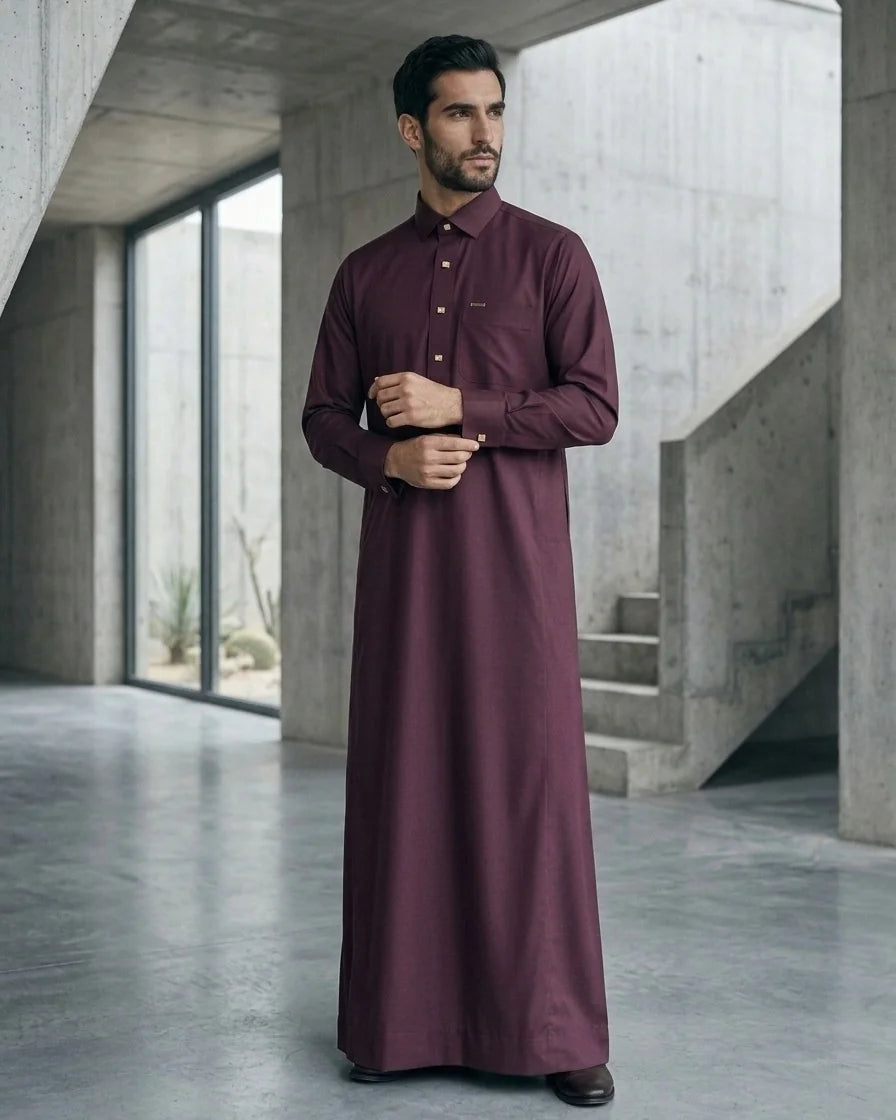 Full length standing pose in rich maroon executive thobe with gold buttons, chest pocket badge and cuffed sleeves in modern architecture — The Topiwala