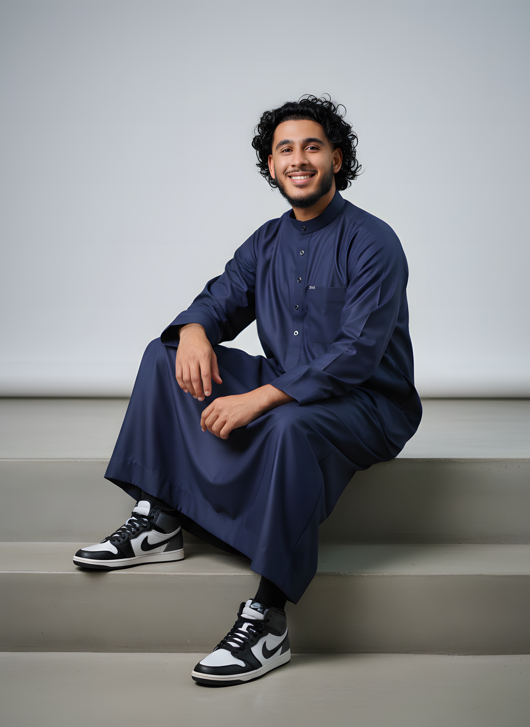 Young man wearing a modern navy blue tailored thobe styled with sneakers for a casual, urban Islamic look.