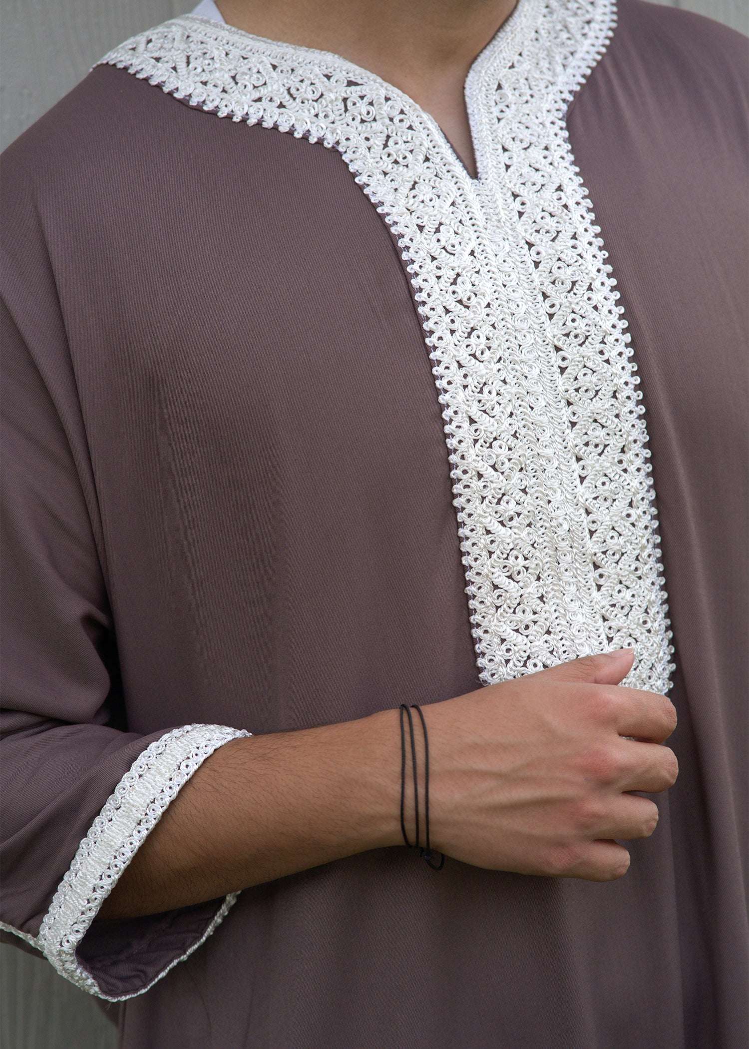 Close up of the intricate white embroidery on the chest and neckline of the taupe men's thobe