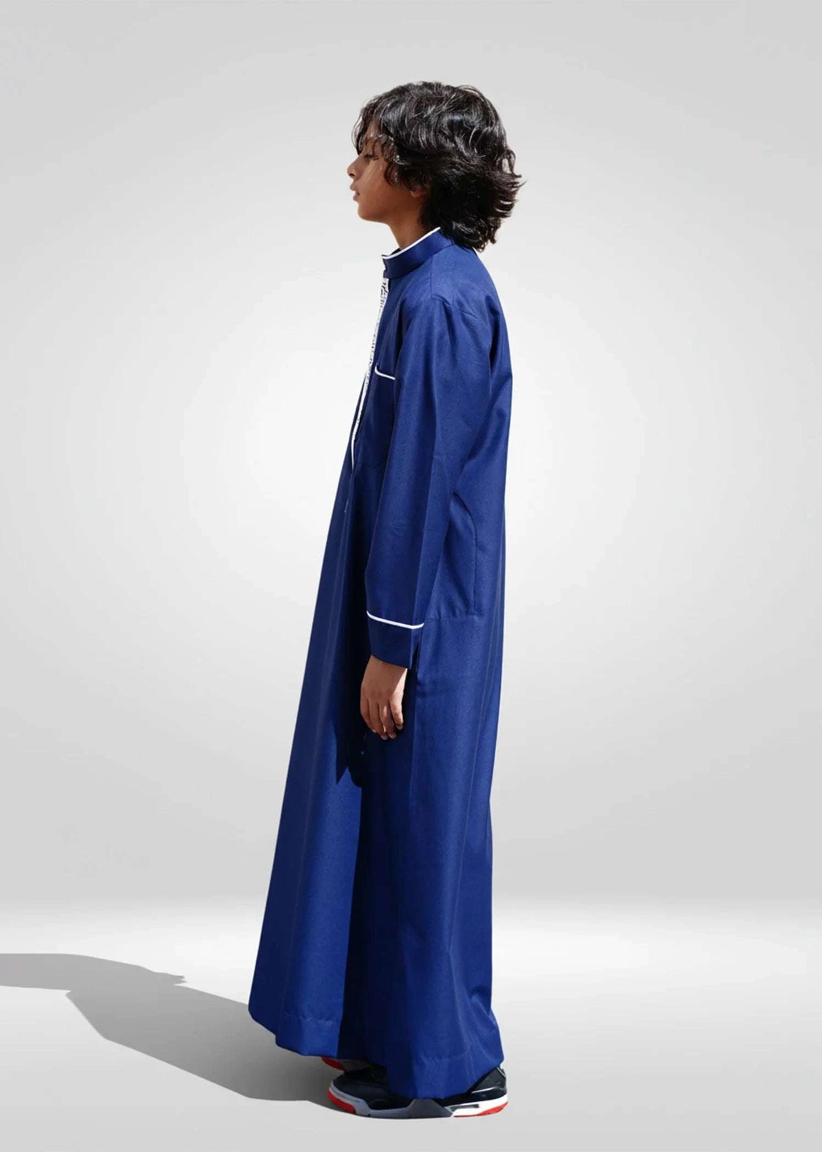 Navy blue embroidered thobe for boys, worn by a model outdoors