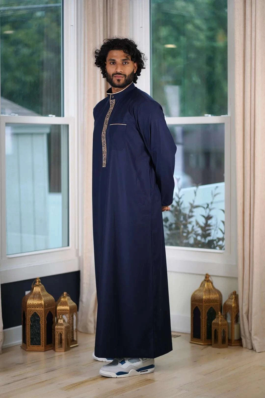 Lifestyle shot of a man wearing the navy and beige embroidered thobe, looking elegant for a special event