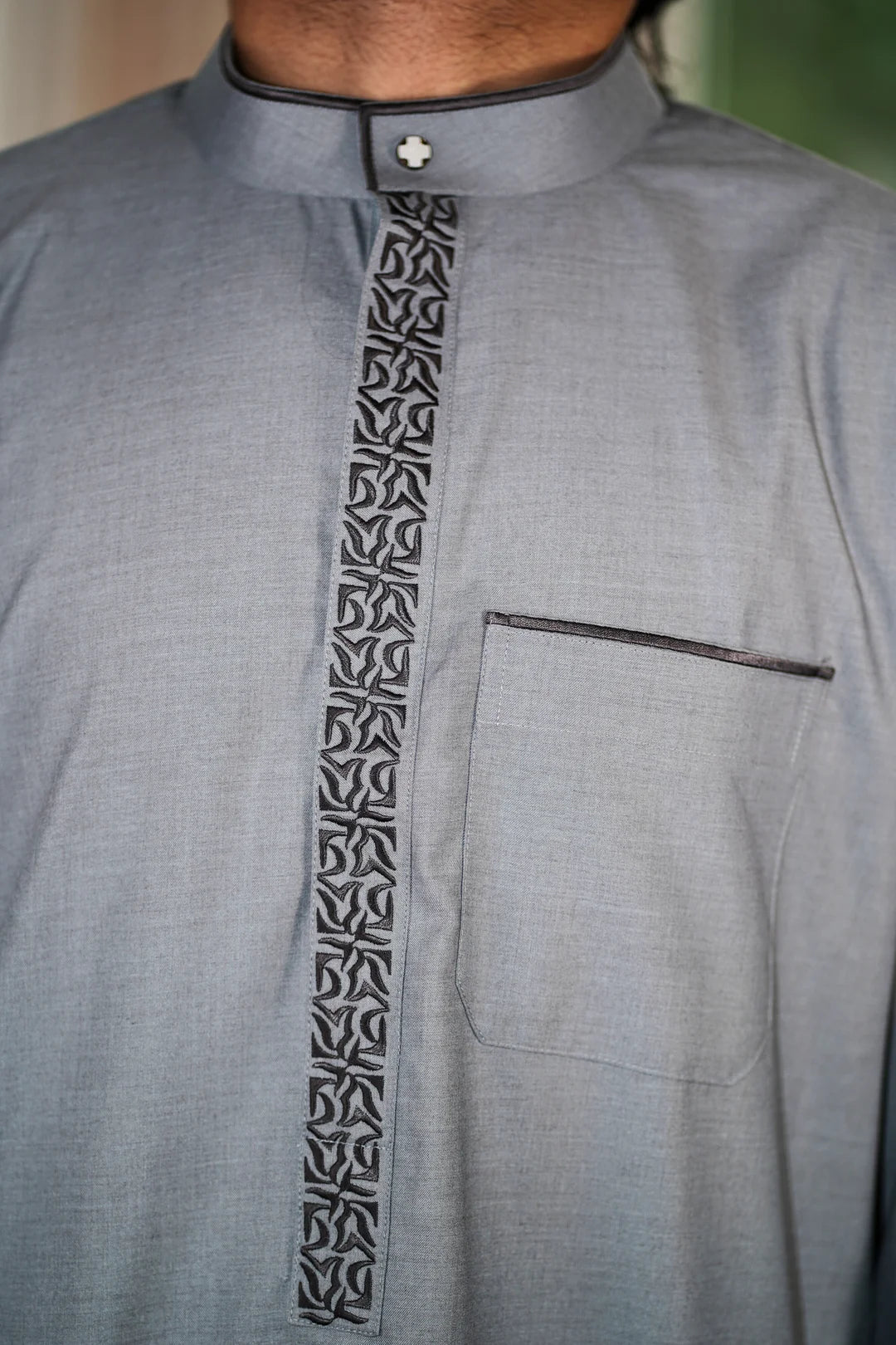 Close up of the intricate charcoal embroidery on the chest and mandarin collar of the gray men's thobe