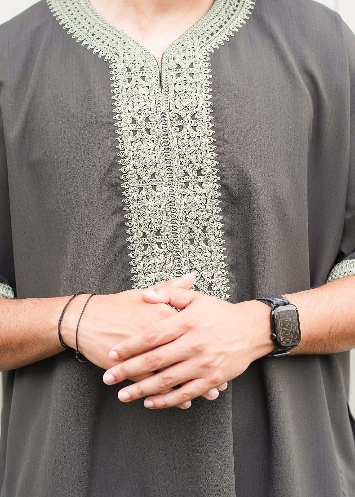 Close-up shot of the intricate, tonal light olive green embroidery running down the chest placket and neckline of the thobe.