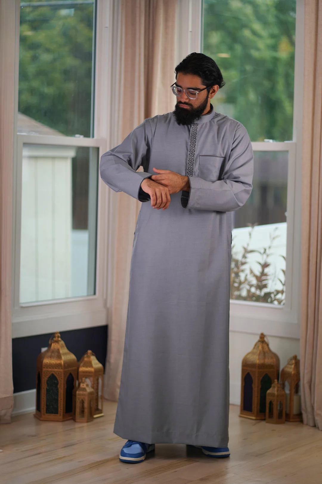 Lifestyle shot of a man wearing the gray and charcoal embroidered thobe, looking elegant for a special event