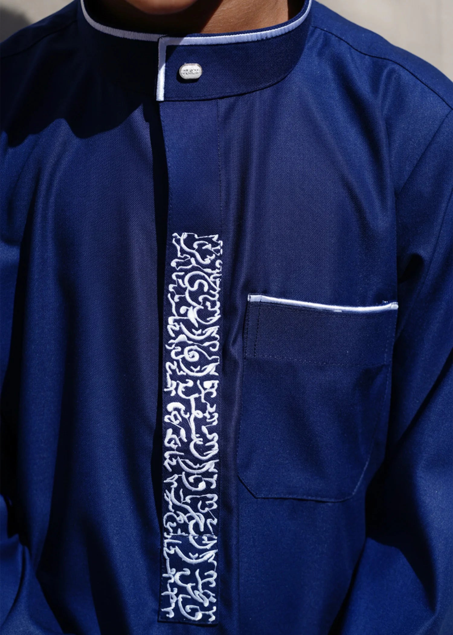 Close up of the intricate white geometric pattern on the chest and collar of the navy boys thobe