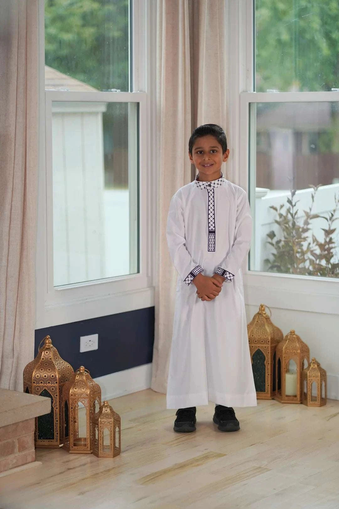 White jubba with Kufiya embroidery for boys, worn by a model outdoors
