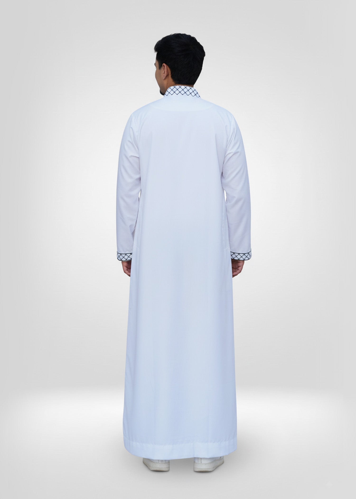 Lifestyle shot of a man wearing the white and black embroidered thobe, looking proud and stylish