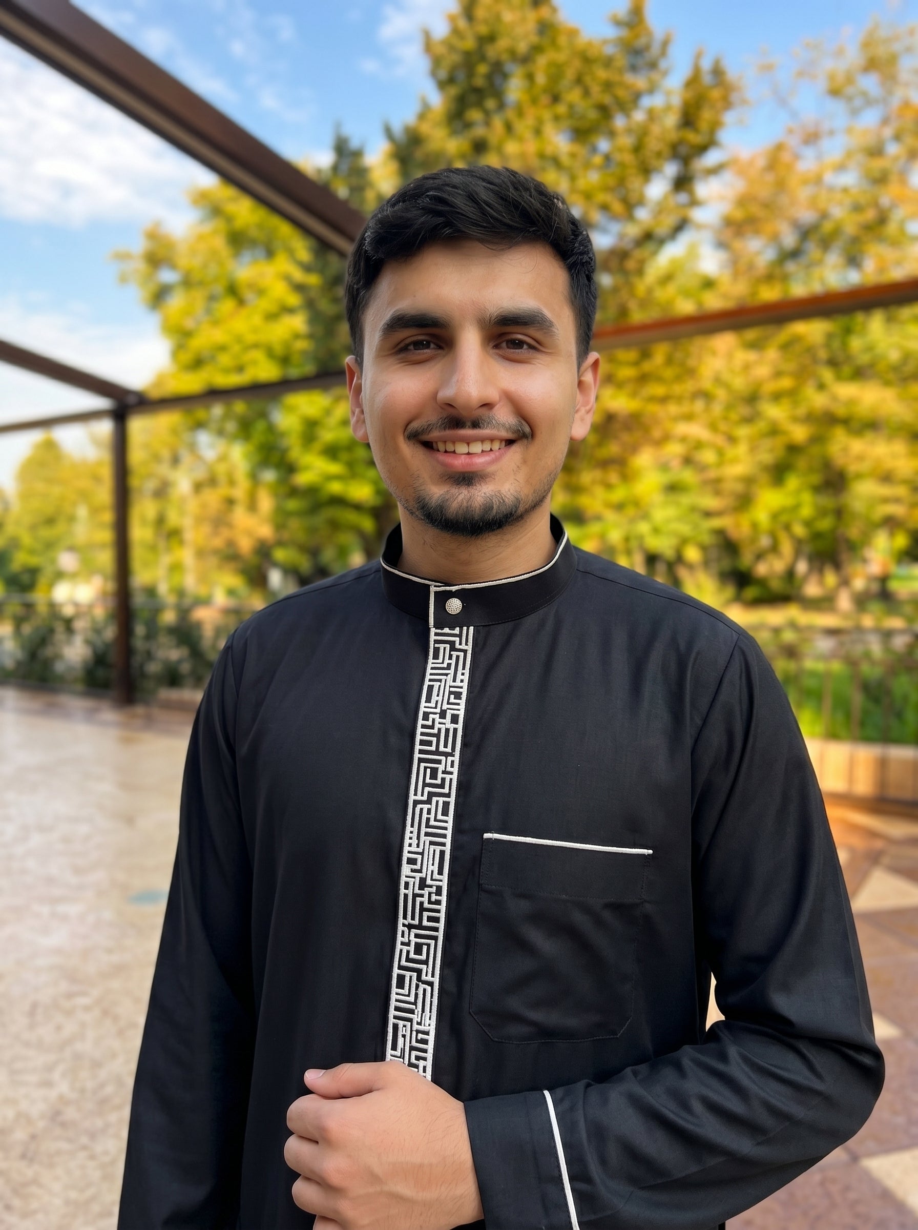 Luxury black jubba with white embroidery leaning against a pergola, professional modest fashion photography inspired by Shukr and Burda clothing, The Topiwala Chicago online store.