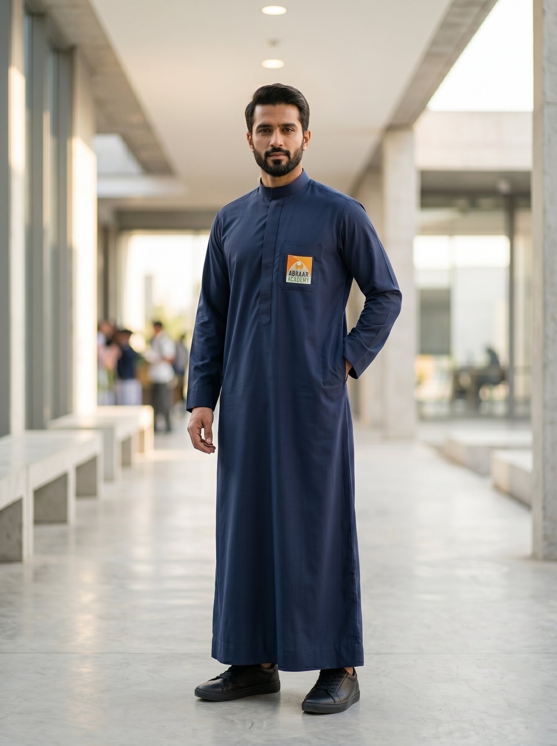 Adult male wearing the official Abraar Academy navy blue men's uniform thobe with chest logo, showcasing a tailored architectural fit in a modern setting.