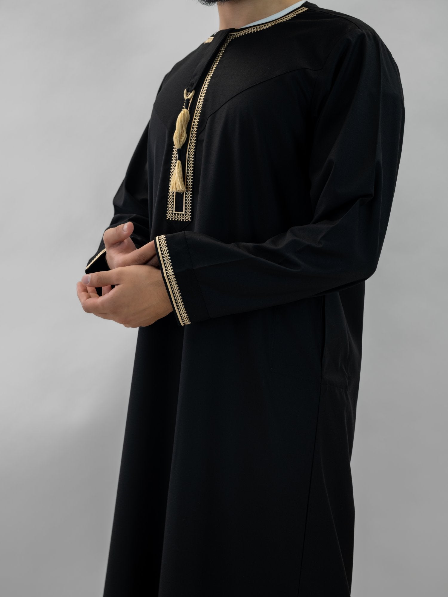 Black emirati gold trim tarboush thobe for men and boys, worn by a model outdoors
