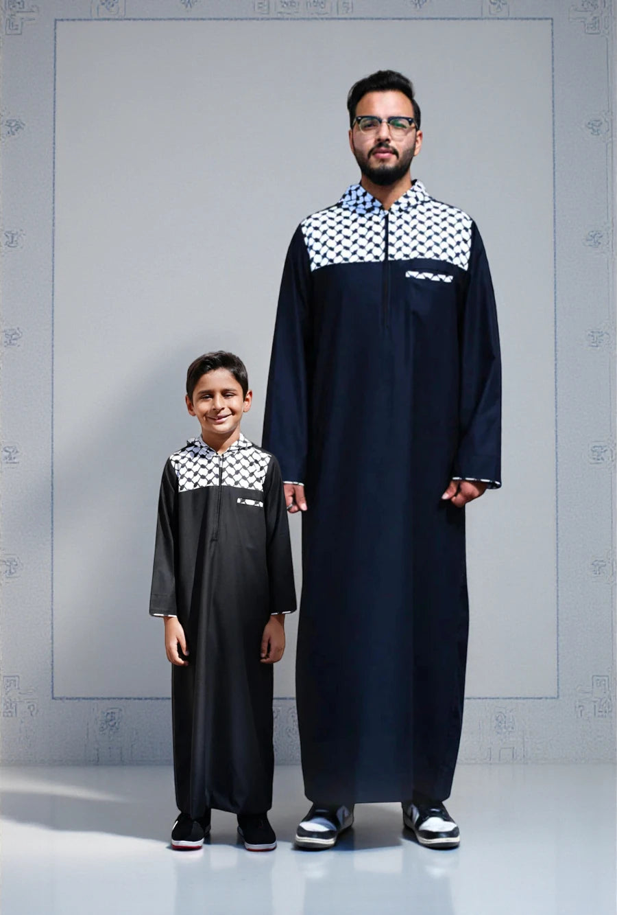 The Topi Wala matching Father and Son set featuring the Black Palestine Hoodie Thobe. A modern streetwear-inspired jubbah with the iconic white and black Kufiya (keffiyeh) pattern covering the hood and upper shoulders. Both father and son stand side-by-side wearing sneakers, showcasing the casual, comfortable fit. Perfect for youth, protests, and casual daily wear.
