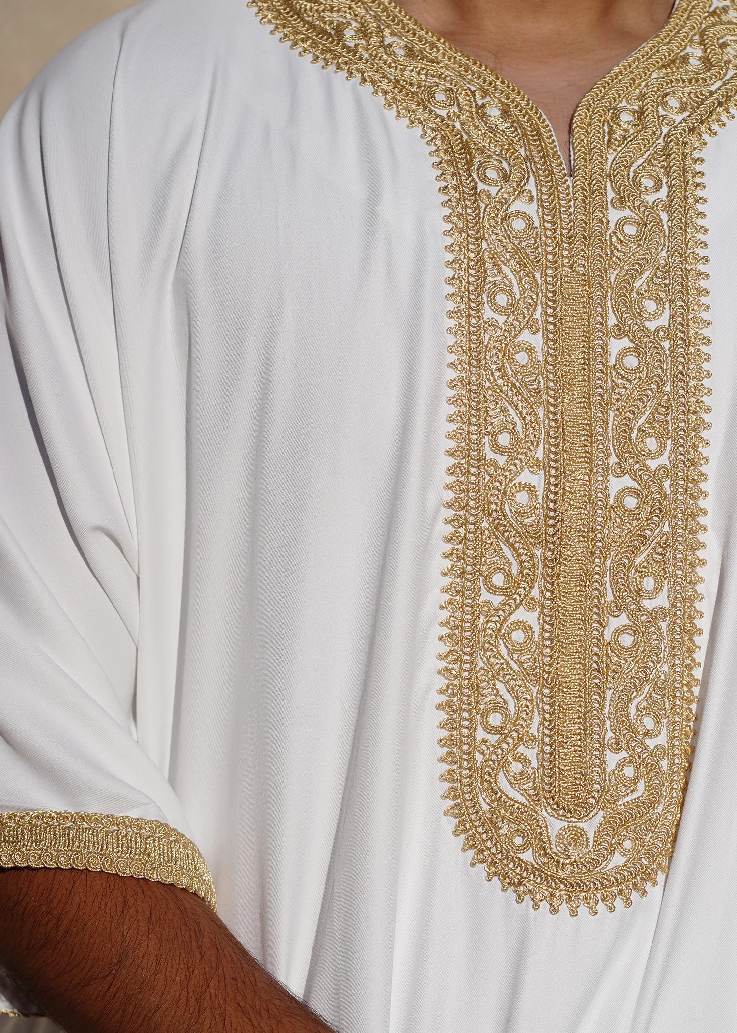 Close up of the intricate gold embroidery on the chest and neckline of the white men's thobe