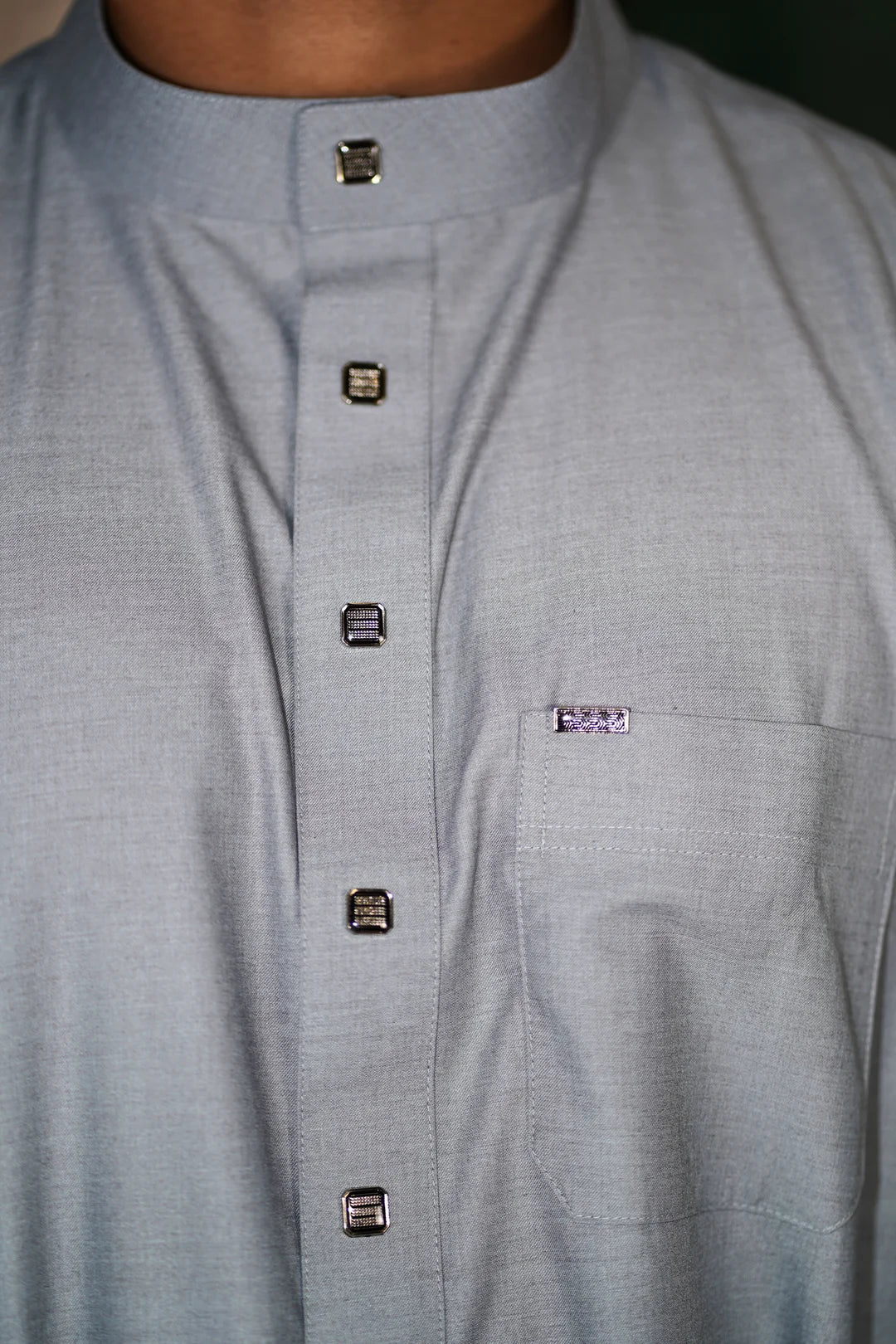 Close up of the mandarin collar and button placket on the light gray boys thobe