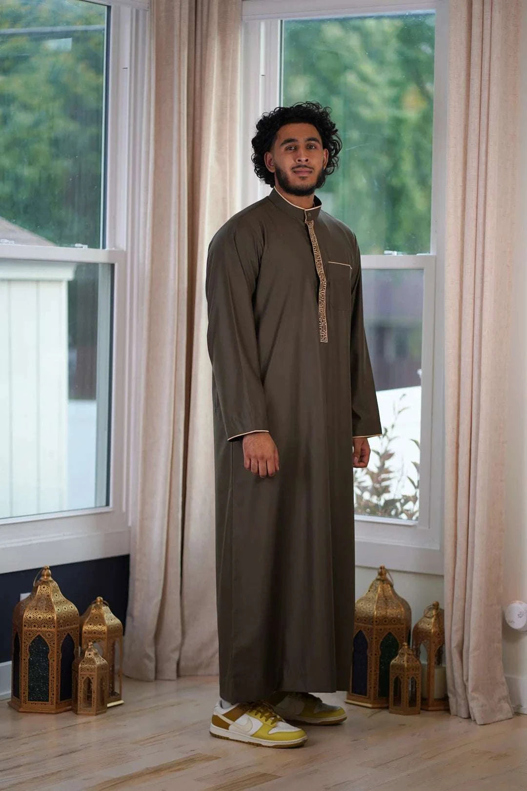 Olive green and gold embroidered thobe for men, worn by a model outdoors