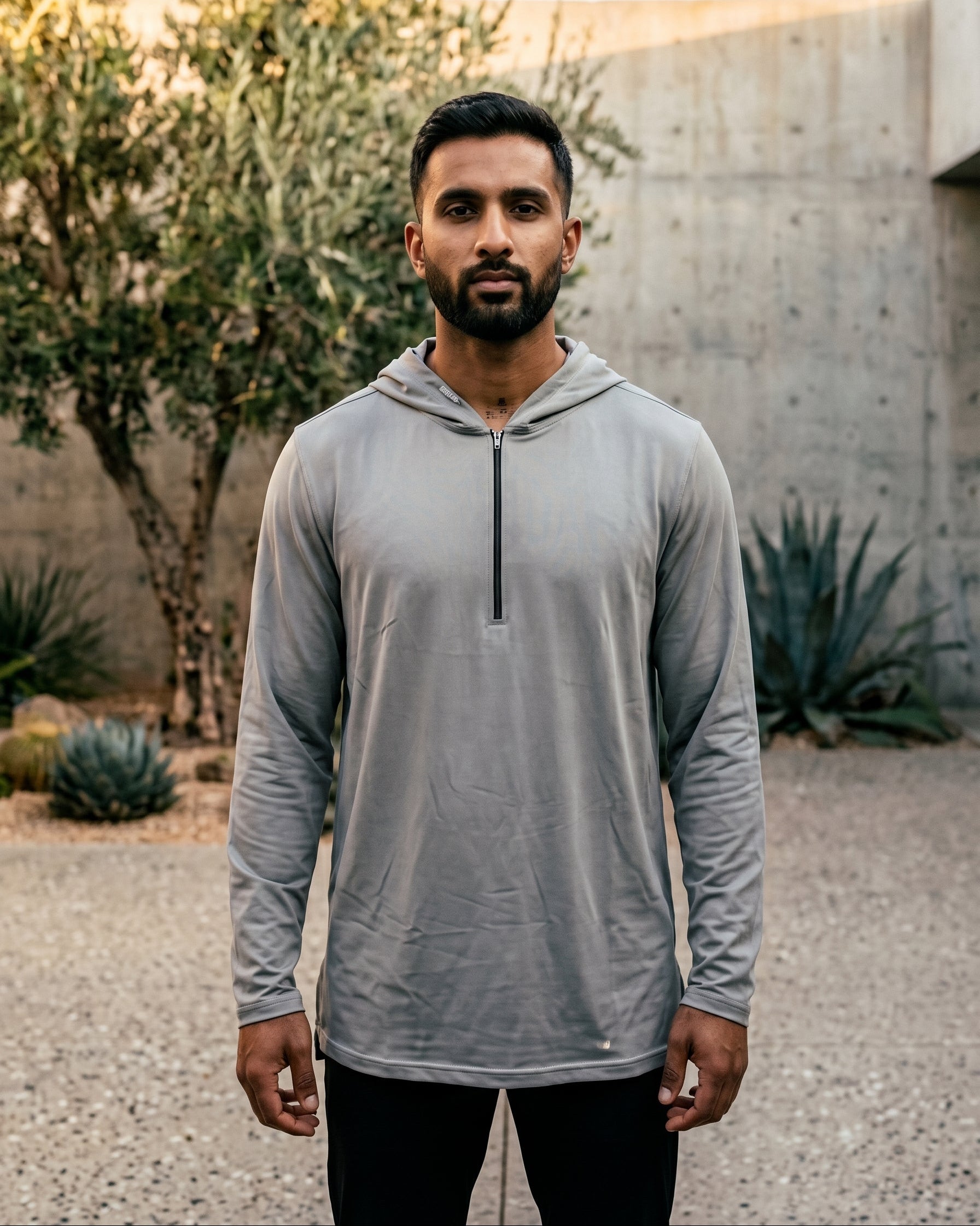 Premium light grey jersey hooded kurta for men sitting on concrete bench, half zip Islamic streetwear, modest casual menswear.